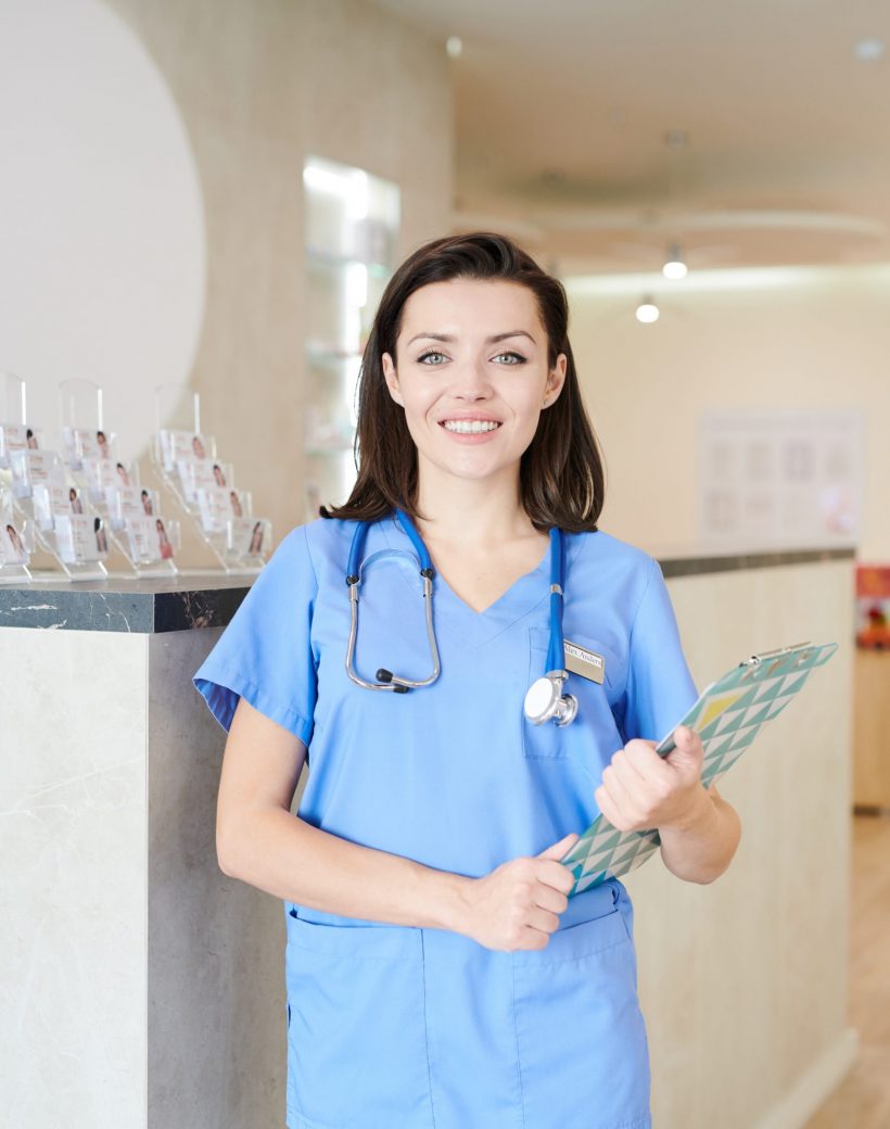 Portrait of  young female doctor looking at camera and smiling cheerfully while posing in hall of modern clinic